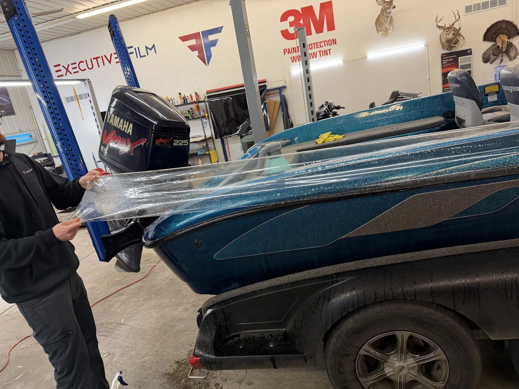 Installer fitting clear paint protection film to a blue fishing boat